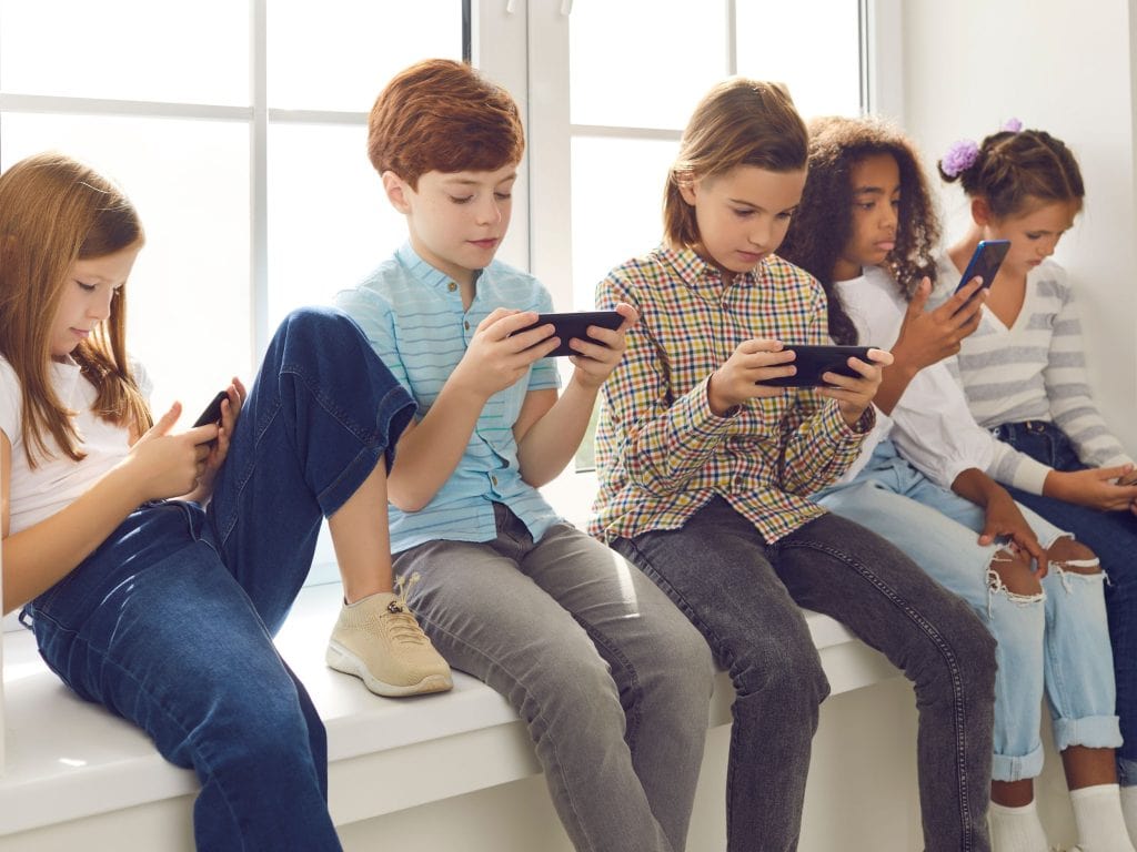 Group of teenagers texting  mobile phone messages leaning against urban  wall - Row of best student friends using smartphone wearing summer trendy clothing.