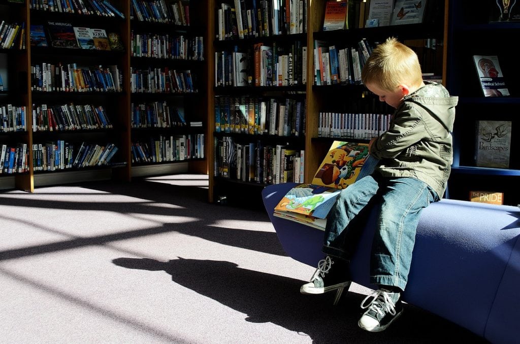 Young boy reading a picture book, sitting on a bench surrounded by bookshelves