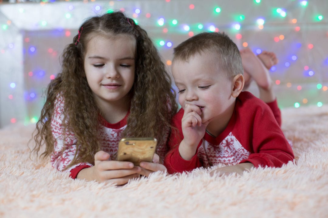 Kids in Christmas clothes looking at a cell phone