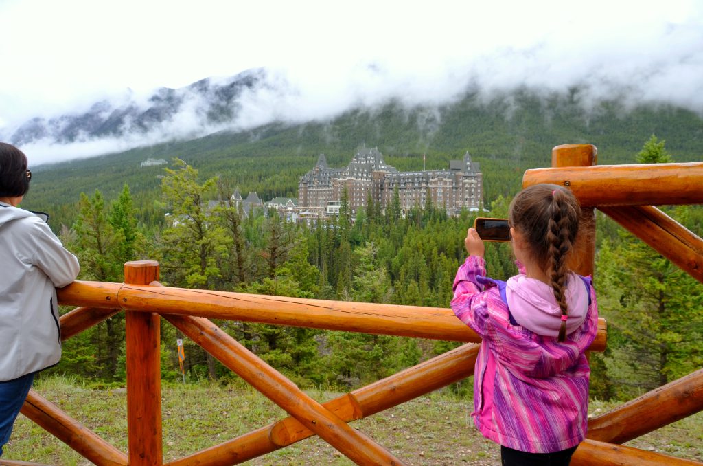 Girl taking a picture of Banff Springs from Surprise Corner in Banff