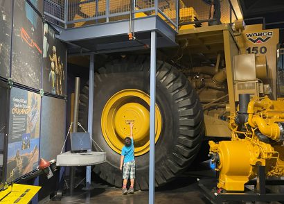 Little boy stretches to touch the hubcap of a WABCO 150 Heavy Hauler at Oil Sands Discovery Center in Fort McMurray