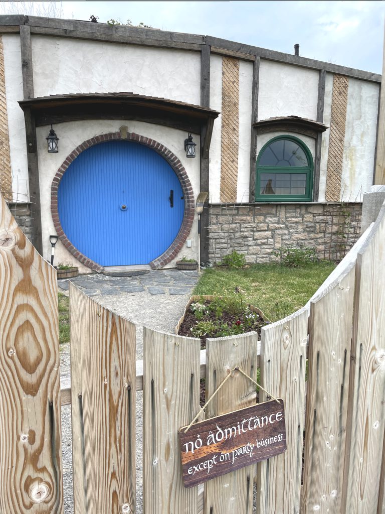 Front entrance to The Burrow with bright blue round door. A sign on the gate reads "no admittance except on party business."