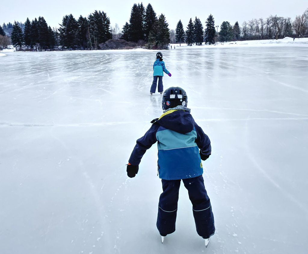 Two kids ice skating on the pond in Hawrelak Park, Edmonton.