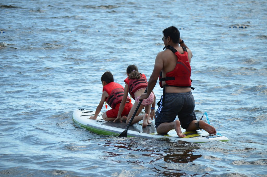 Kids and dad in PDFs share a Beyond Adventures paddle board on Gregoire Lake.