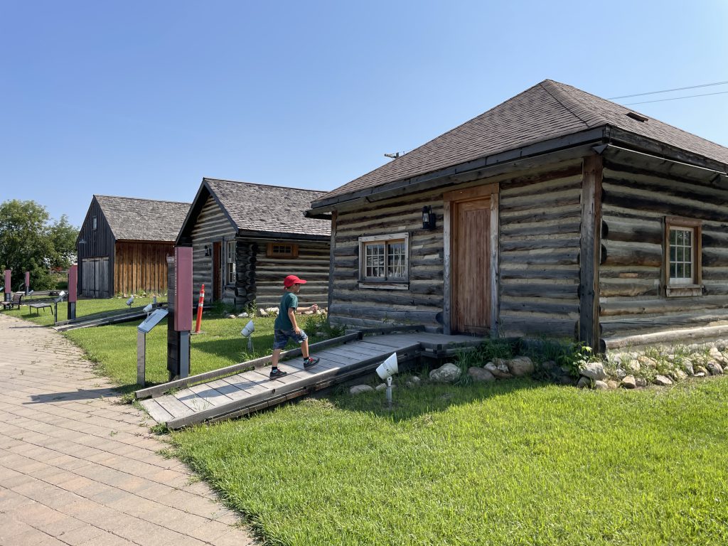 Young boy approaches the door of the first of three log cabins in Heritage Village, Fort McMurray