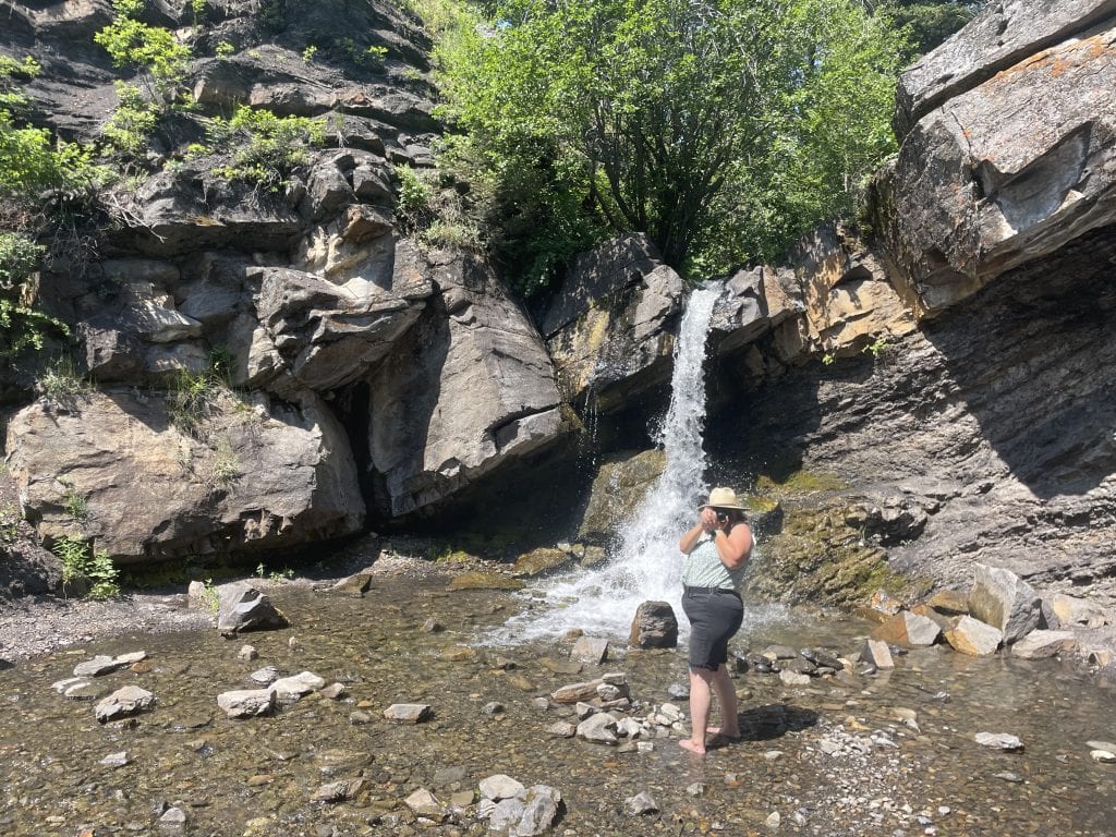 Woman taking a photo of the photographer with Rainbow Falls at the end of Miner's Path in the background.